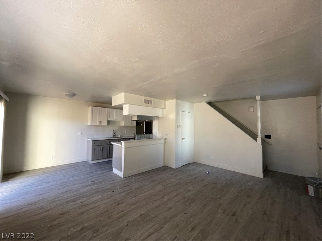 Vacant open-plan living area with a compact kitchen, breakfast bar, and staircase.