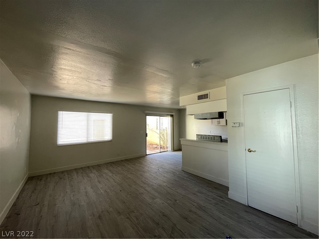 Vacant living room and kitchen with gray wood-look floors, a wide window, and sliding glass door.