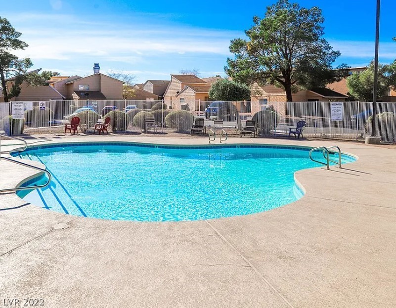 Community swimming pool with a fenced deck, lounge chairs, and townhomes beyond.