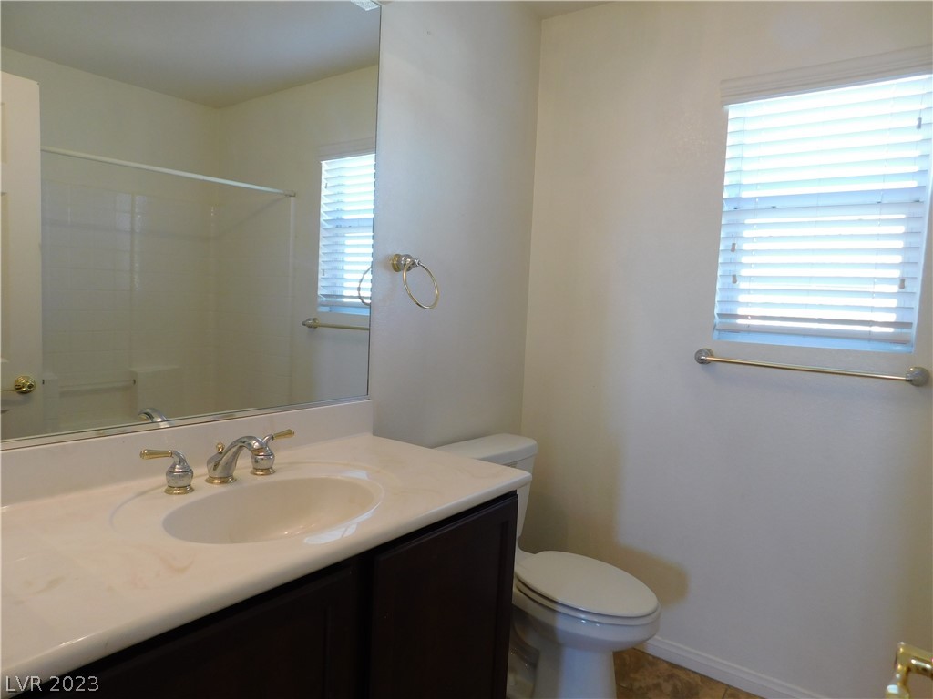 Bathroom with dark wood vanity, large mirror, toilet, and a window with white blinds.