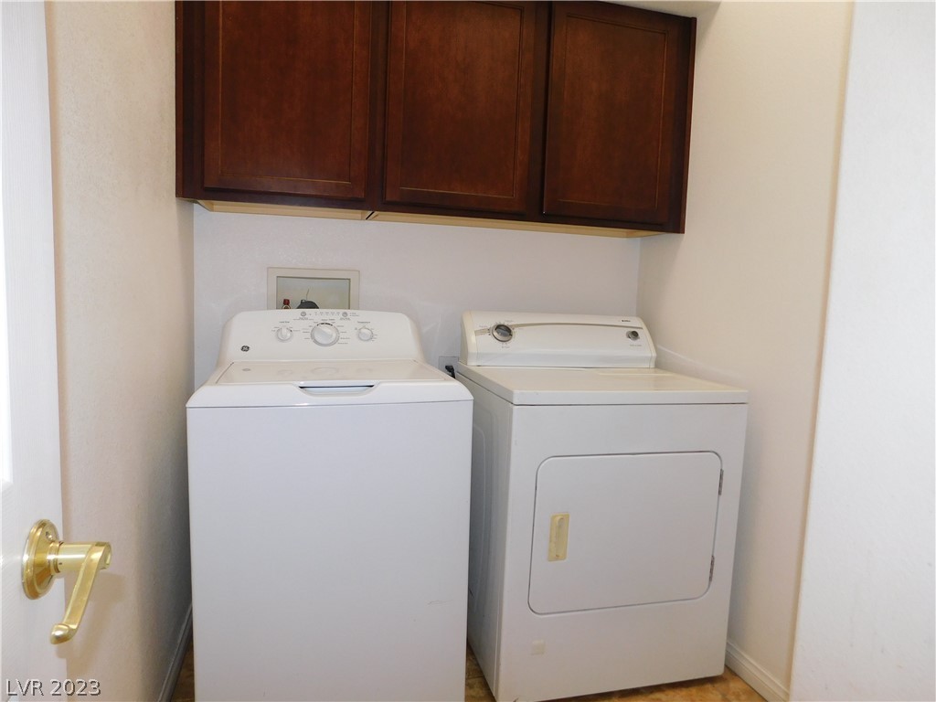 Laundry room with a white washer and dryer beneath dark wood cabinets.