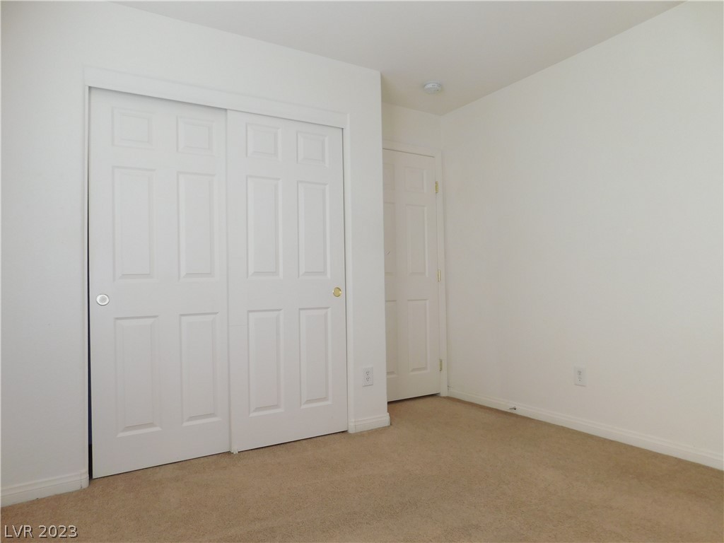 Vacant bedroom with beige carpet, white sliding closet doors, and a separate hinged door.
