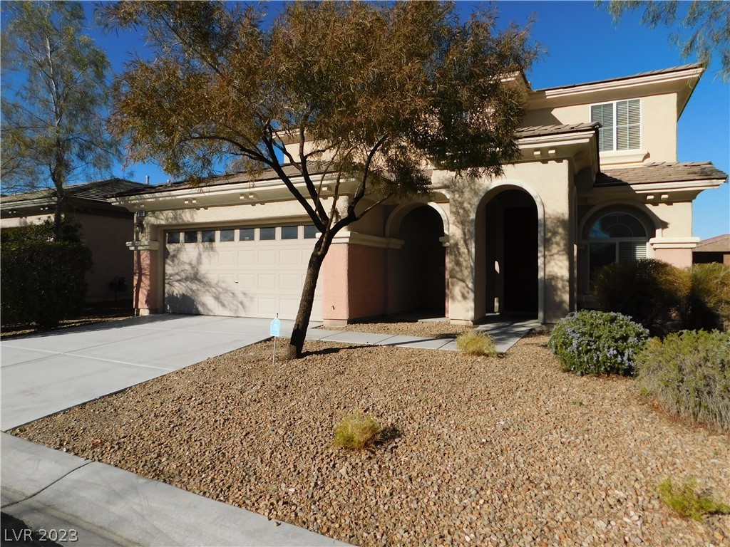 Two-story stucco home with an attached garage, arched entryways, and desert landscaping.