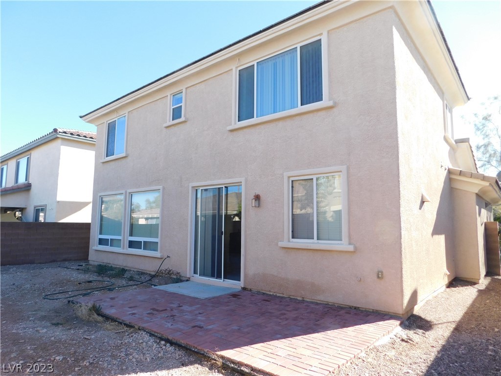 Rear of a two-story stucco home with a brick patio and gravel yard.