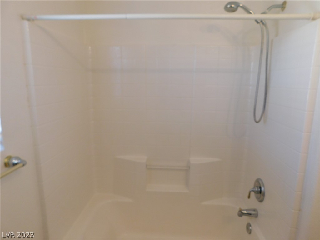 White bathtub and shower alcove with a built-in shelf and chrome fixtures.