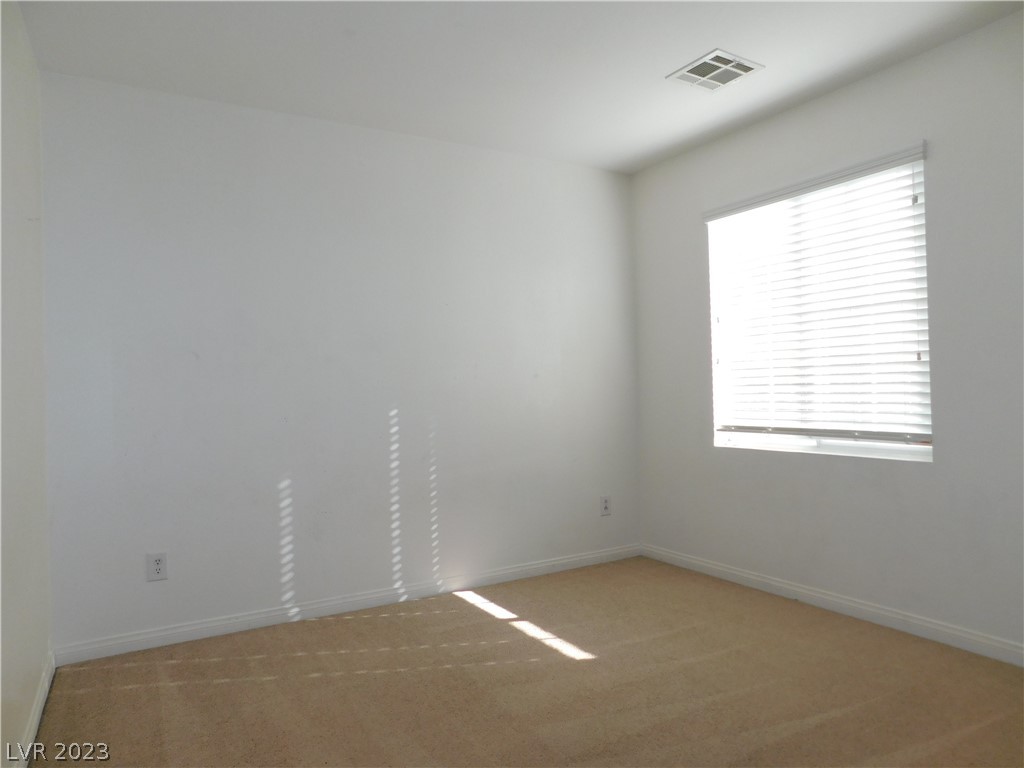 Empty carpeted room with white walls and a sunlit window with blinds.