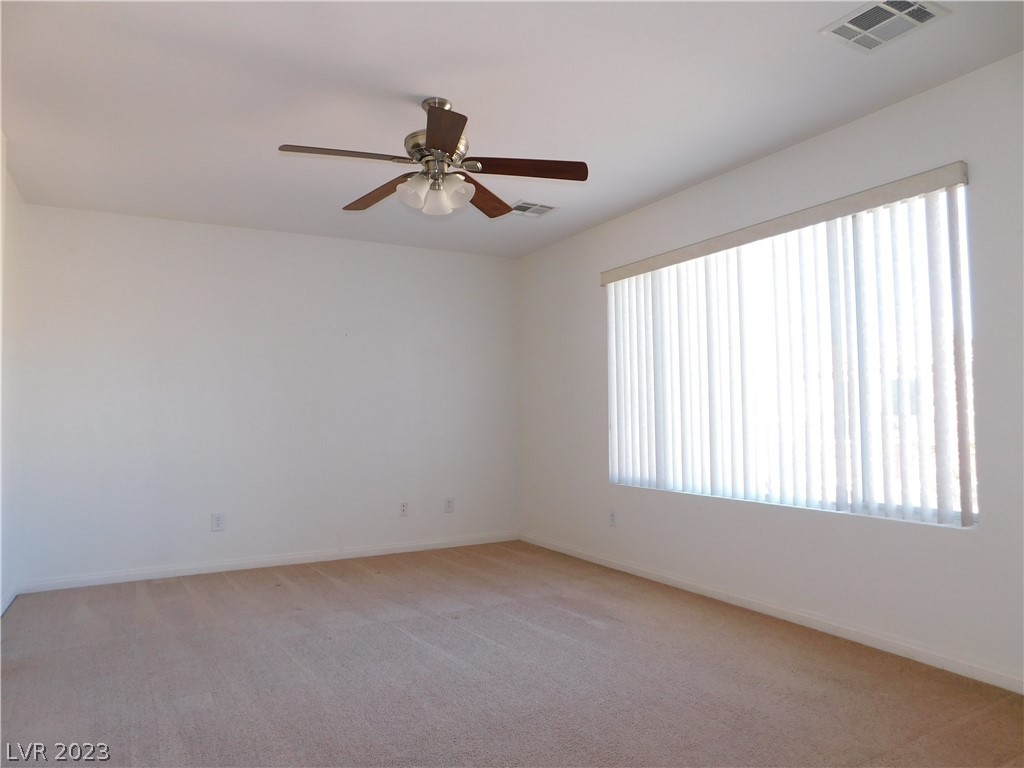 Empty carpeted bedroom with a ceiling fan and a large window with vertical blinds.