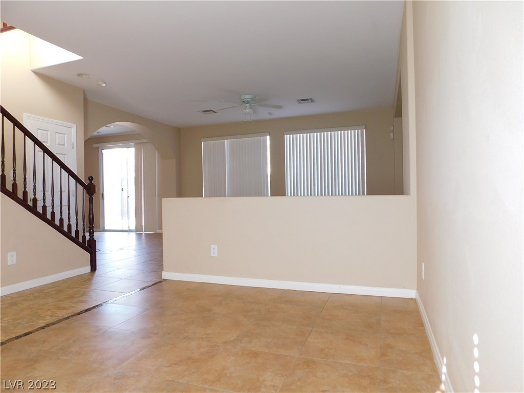 Vacant living area with tan tile floors, a dark wood staircase, and window blinds.