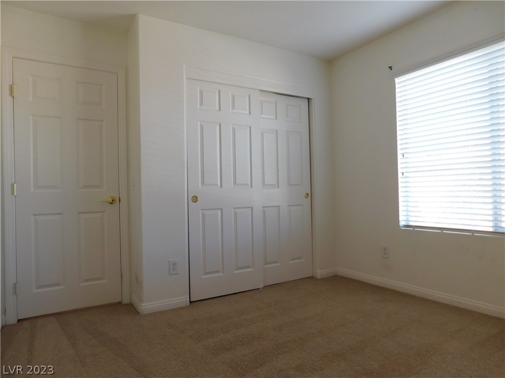 Vacant bedroom with beige carpet, a built-in closet, and a window with white blinds.