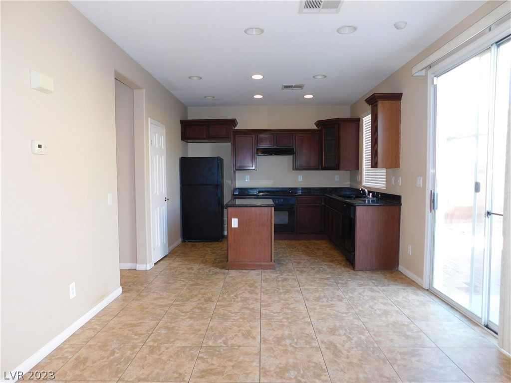 Empty kitchen with dark wood cabinets, black appliances, tan tile flooring, and a sliding glass door.