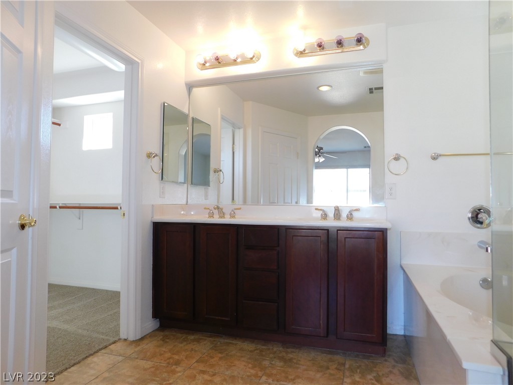 Bathroom with a dark wood double vanity, wide mirror, and adjoining soaking tub.