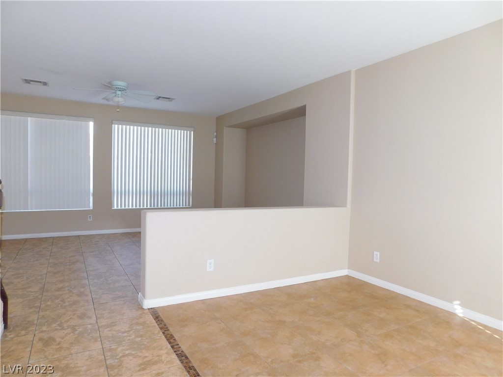 Vacant living and dining area with tan tile floors, vertical blinds, and a half-height partition.