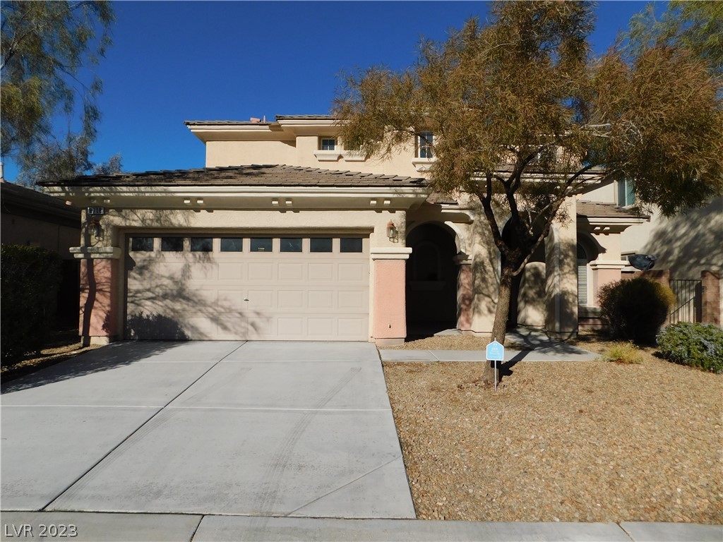 Two-story stucco home with a tile roof, two-car garage, and mature tree by the covered entry.