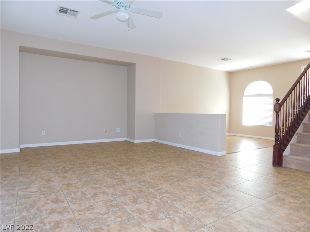 Vacant living room with tan tile floors, a half wall, and a carpeted staircase.