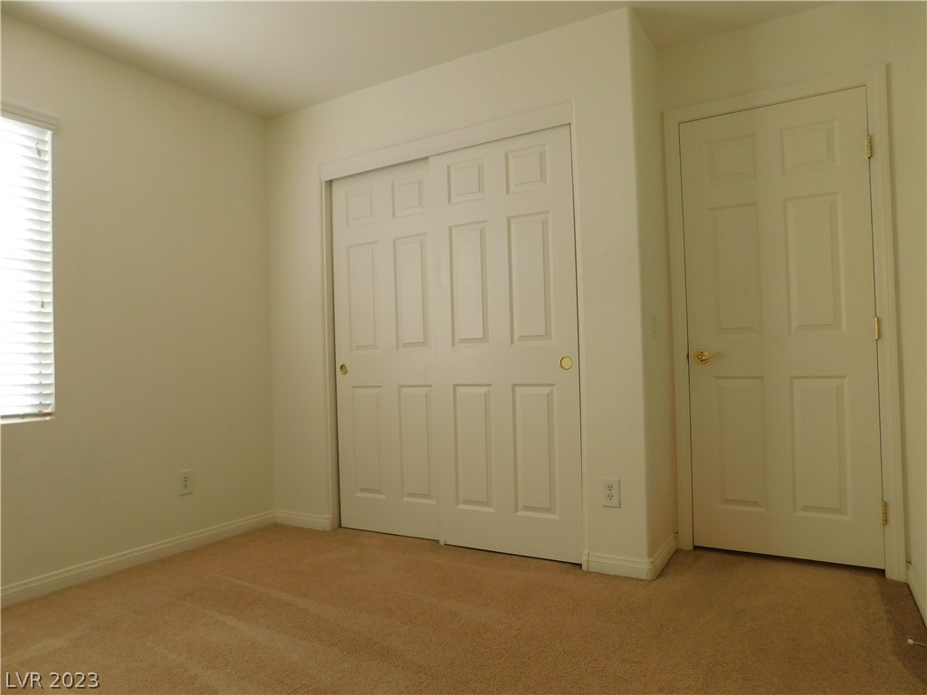 Empty carpeted bedroom with a window and blinds, sliding closet doors, and a separate hinged door.
