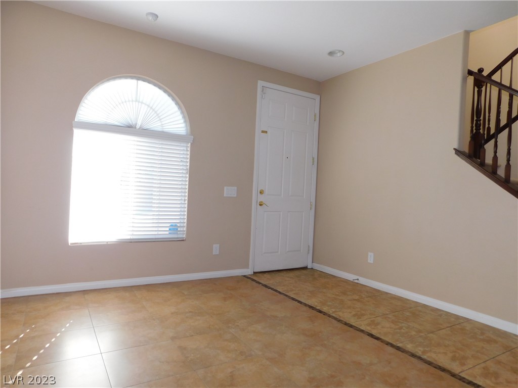 Empty entry with tan tile, a white front door, an arched window, and a staircase railing.