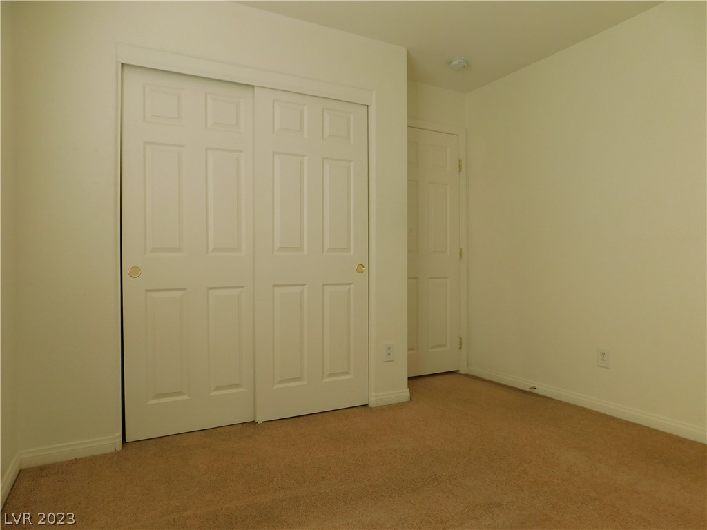 Empty carpeted room with white sliding closet doors and a separate hinged door.