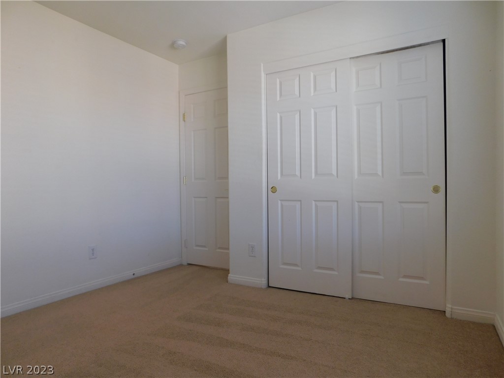 Empty bedroom with beige carpet, white walls, and white double closet doors.