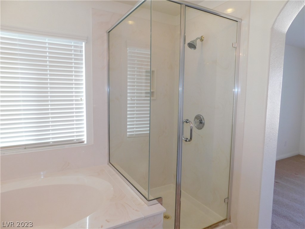 Bathroom with glass-enclosed shower beside a built-in tub and a window with white blinds.
