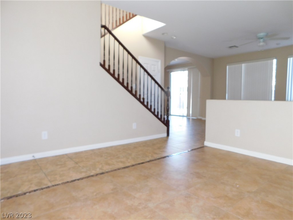 Vacant living area with tan tile floors, a dark-railed staircase, and an arched opening.