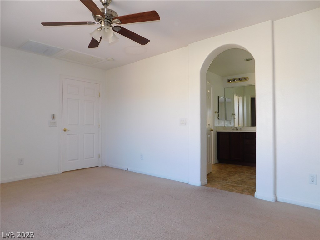 Empty carpeted bedroom with a ceiling fan and arched doorway to a bathroom.