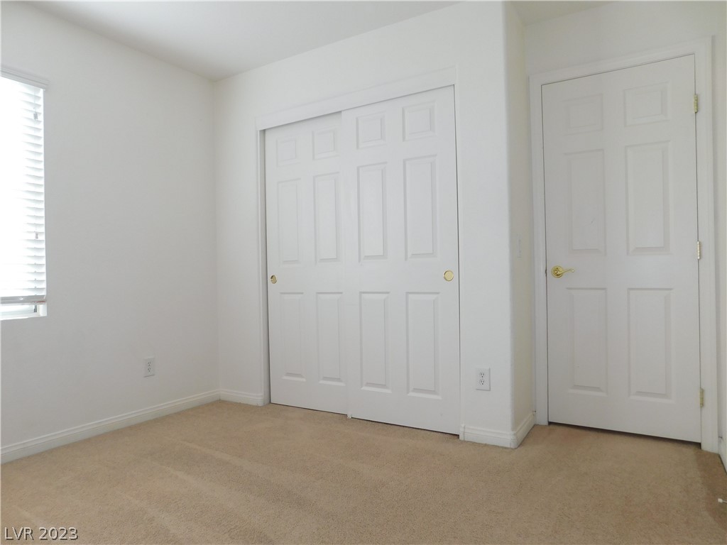 Empty bedroom with beige carpet, sliding closet doors, and a window with blinds.