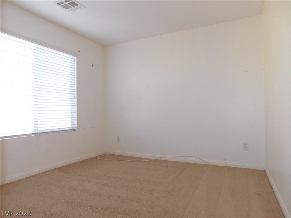 Empty bedroom with beige carpet, white walls, and a window with horizontal blinds.