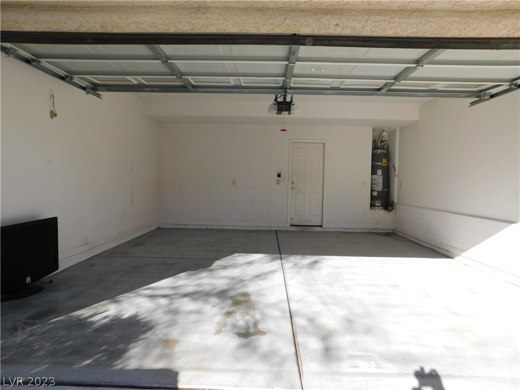 Empty garage with a raised overhead door, concrete floor, and water heater.