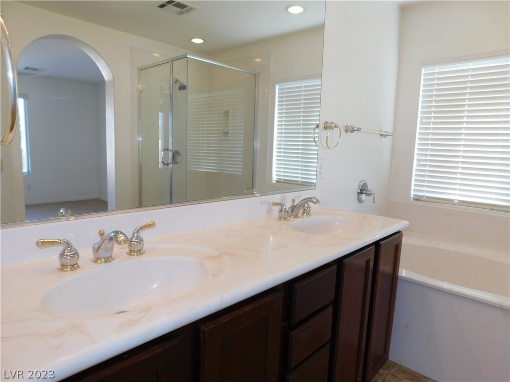 Bathroom with a double-sink vanity, dark wood cabinets, mirrored wall, and glass-enclosed shower.