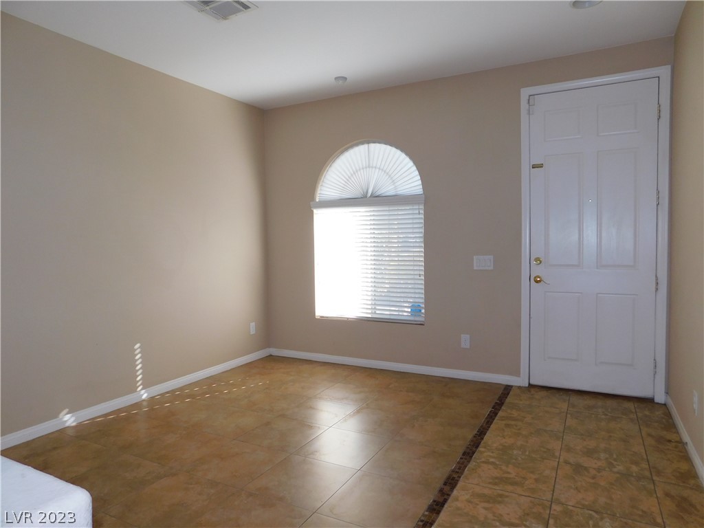 Empty entry area with a white front door, arched window, and tan tile floor.