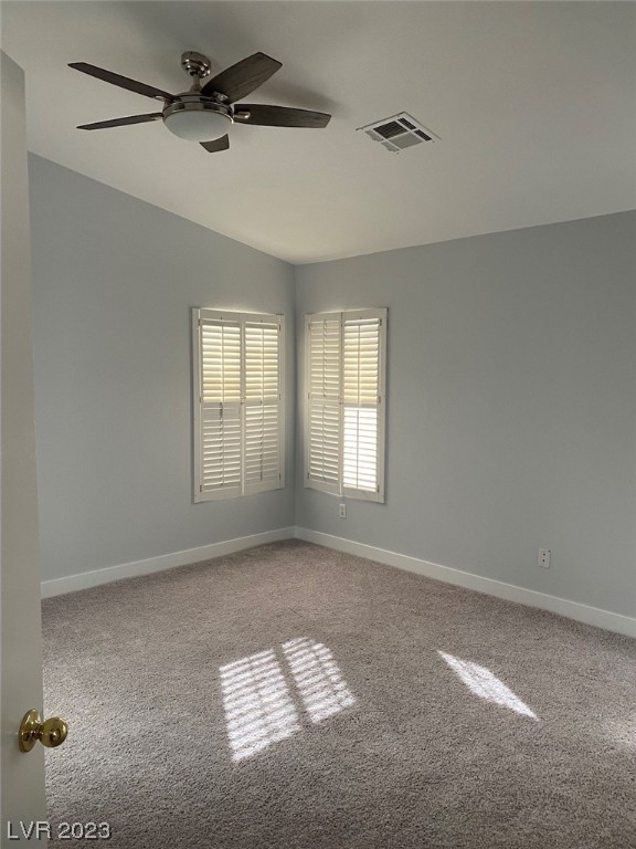 Empty bedroom with beige carpet, two shuttered windows, and a ceiling fan.