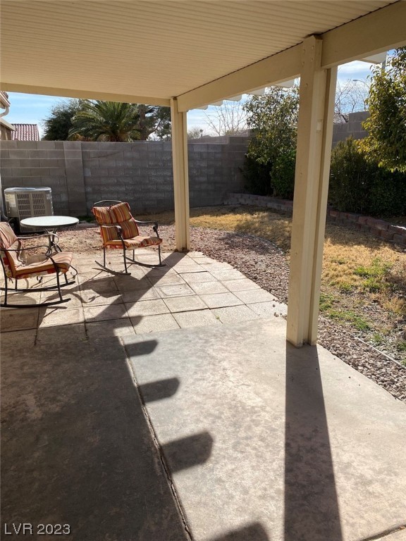 Covered backyard patio with two chairs, a concrete slab, and a walled yard.