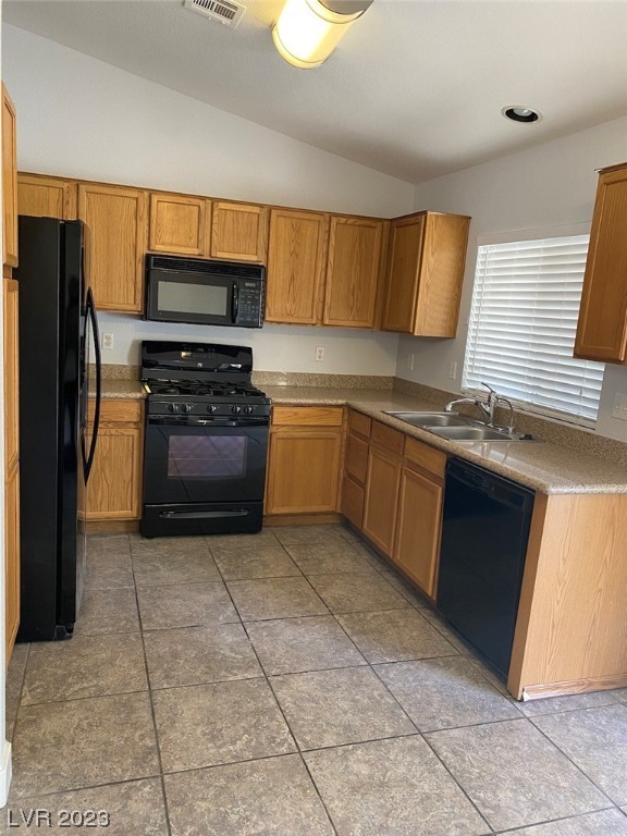 Kitchen with oak cabinets, black appliances, and large square tile flooring.
