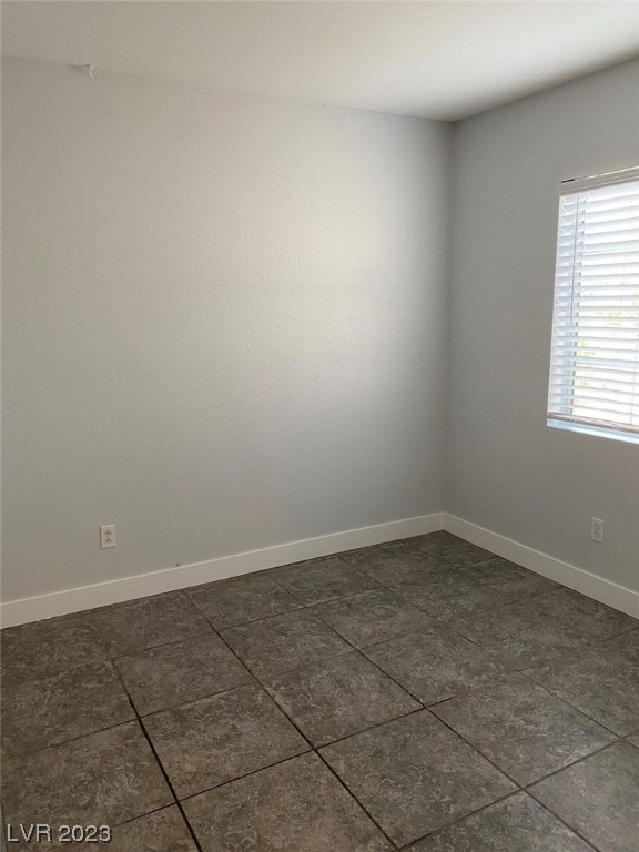 Empty room with dark tiled flooring, gray walls, and a window with white blinds.