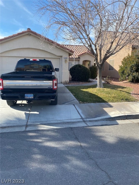 Single-story stucco home with a red tile roof, attached garage, driveway pickup, and leafless front-yard tree.