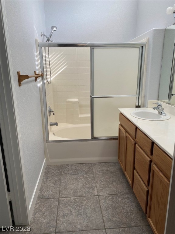 Bathroom with a sliding glass tub and shower, wood vanity, and gray tile floor.