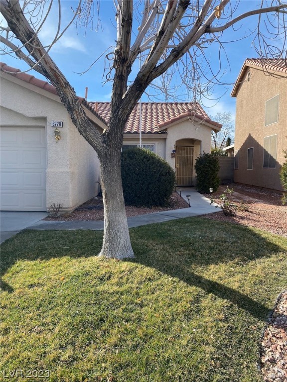 Stucco home with a red tile roof, arched entry, attached garage, and a large leafless tree in the front lawn.