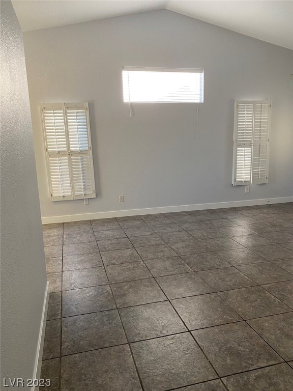 Empty room with dark tile floors, plantation shutters, and a high angled ceiling.