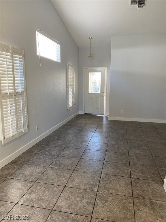 Empty entry room with vaulted ceiling, large gray tiles, plantation shutters, and a glass-panel front door.