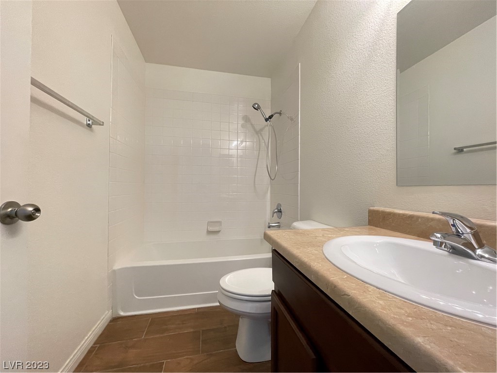 Bathroom with tiled tub and shower, toilet, and dark wood vanity with tan countertop.