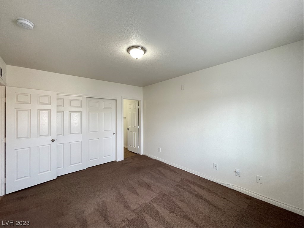 Empty bedroom with brown carpet and several white closet doors.