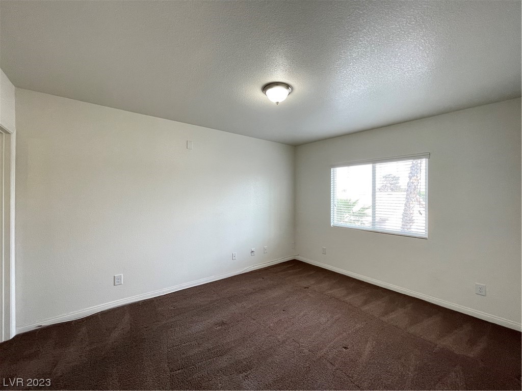 Empty bedroom with brown carpet, white walls, and a window with blinds.