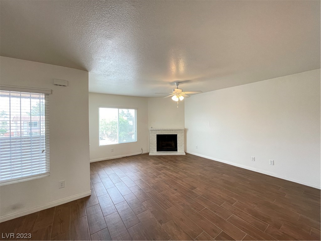 Empty living room with wood-look tile floors, a brick fireplace, and a ceiling fan.