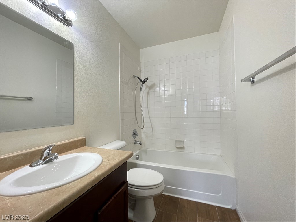 Bathroom with a tiled tub and shower, toilet, and dark wood vanity with a beige countertop.