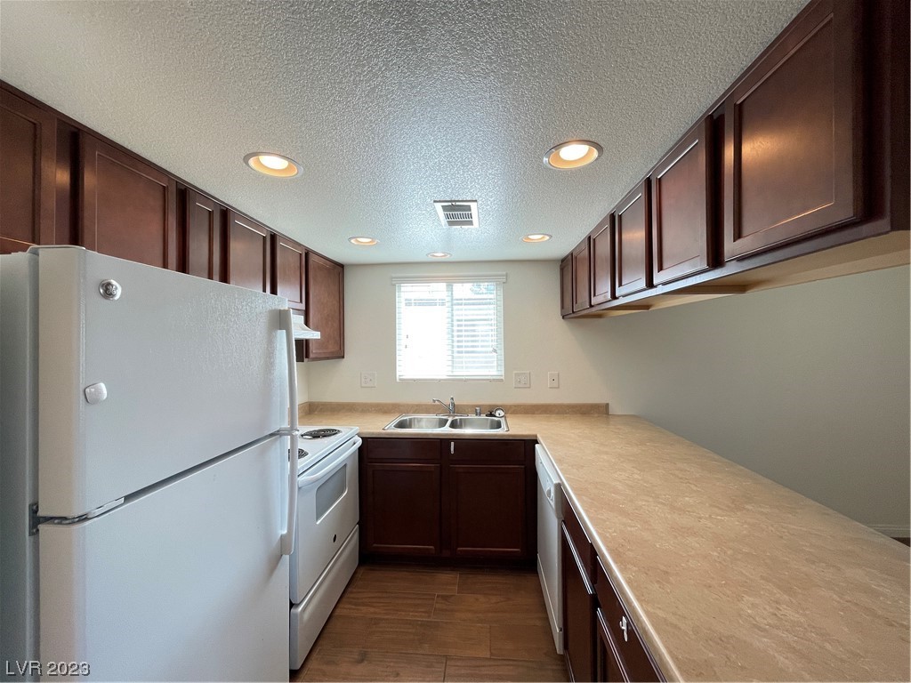 Kitchen with dark wood cabinets, tan counters, and white appliances.