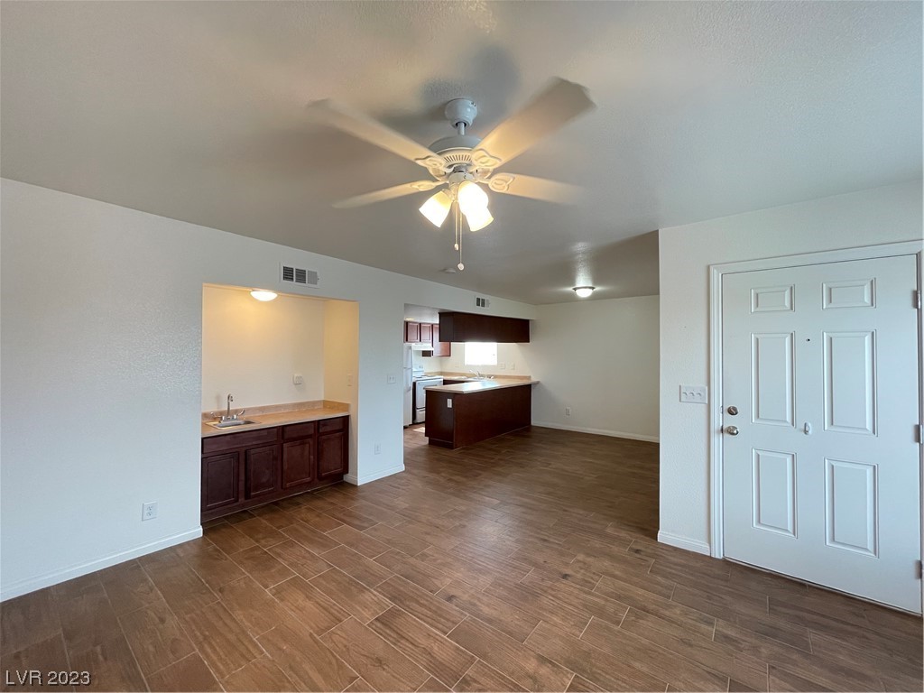 Open-plan kitchen and living area with brown tile floors, dark cabinets, and a ceiling fan.