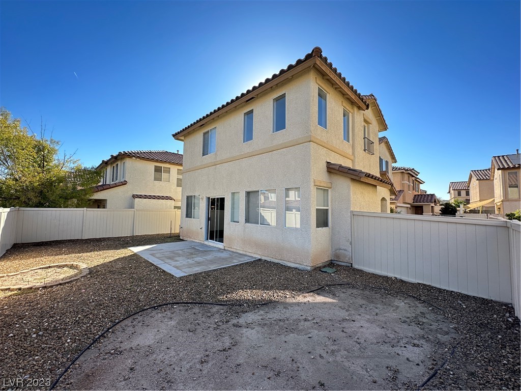 Two-story stucco home with a tiled roof, fenced gravel yard, and small concrete patio.