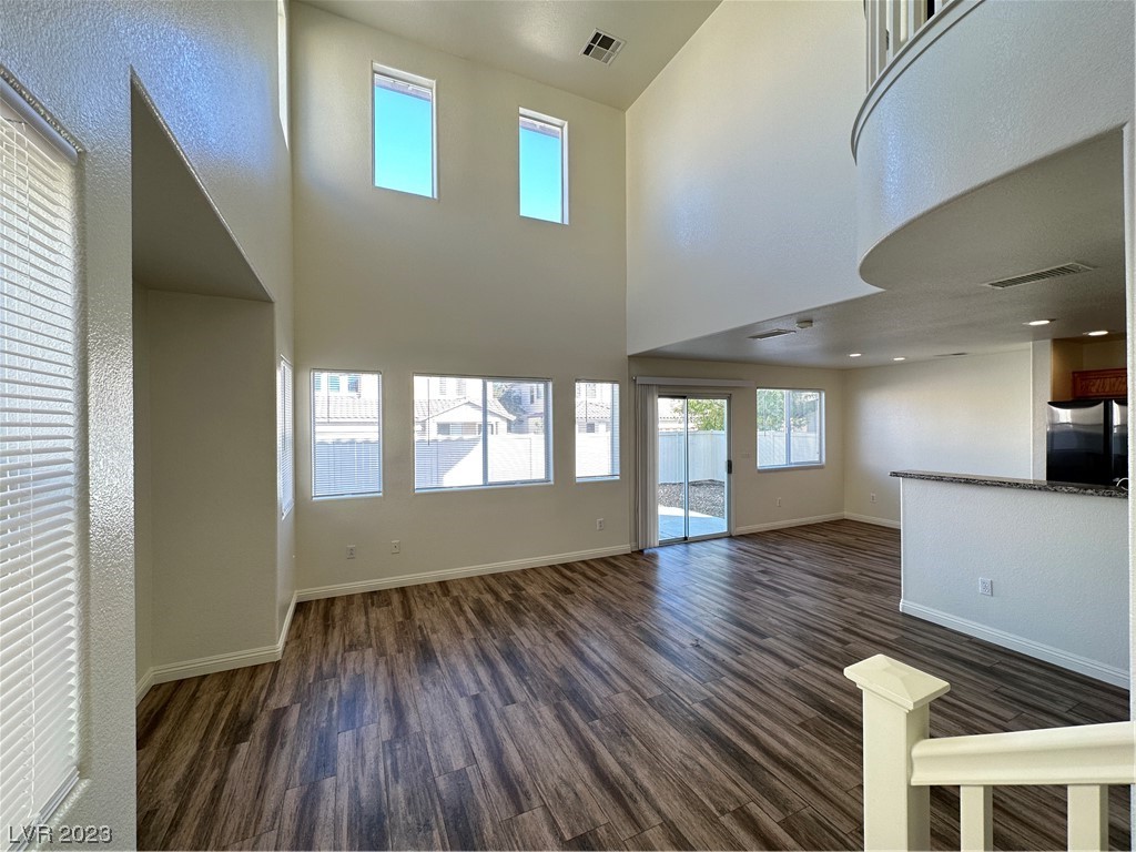 Vacant living room with soaring ceilings, an upper-level overlook, and dark wood-look floors.