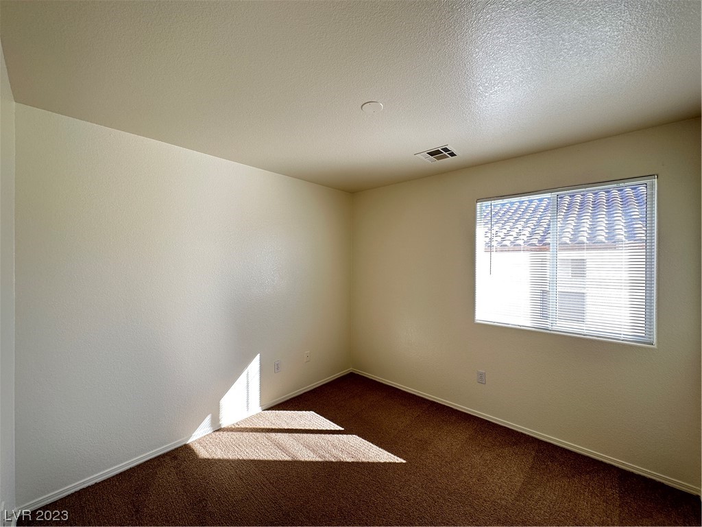 Empty bedroom with brown carpet and a window with blinds, lit by bright sunlight.