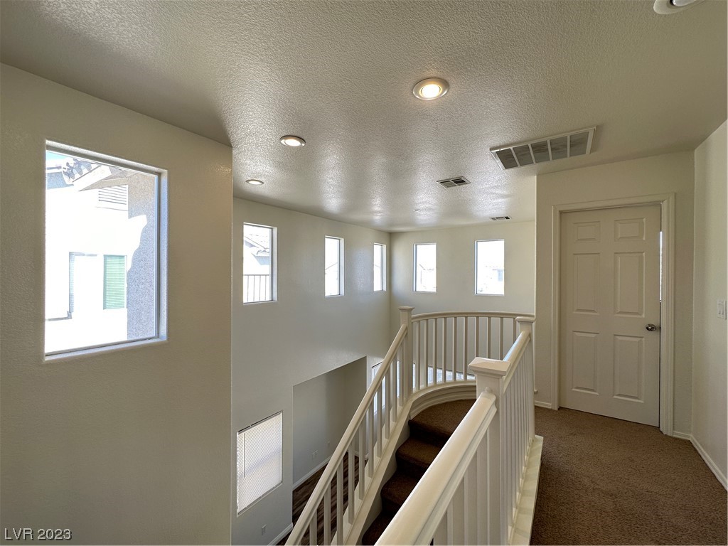 Upstairs landing with a carpeted staircase, white railings, and windows along the wall.